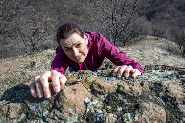 Dişi kaya tırmanışçısı kayalığın tepesine doğru tırmanıyor. Kadın ellerinin kenarda asılı olduğu en iyi manzara. Güç kavramı.