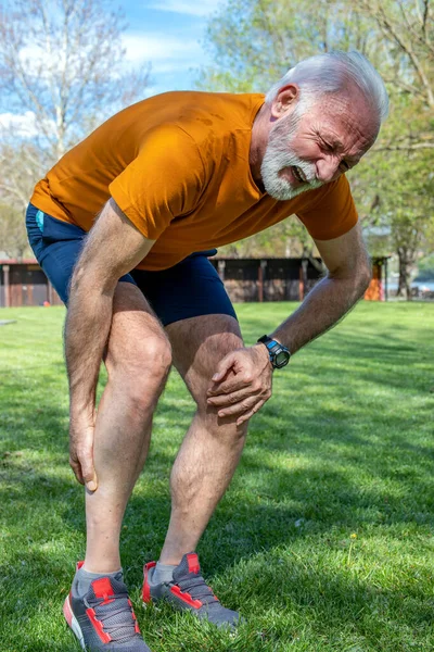 Kıdemli sporcu dışarıda antrenman yaparken kas ağrısıyla kaşlarını çatıyor. Baldıra kramp girdi. Dikey yönelim.
