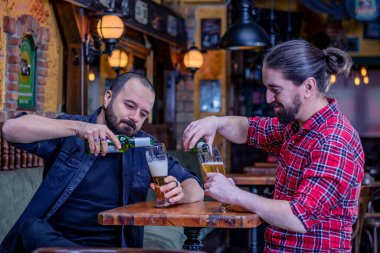 Barda içen iki erkek arkadaş. Şişeden büyük bardaklarda bira dolduruyor. Normal hayata dönüş..