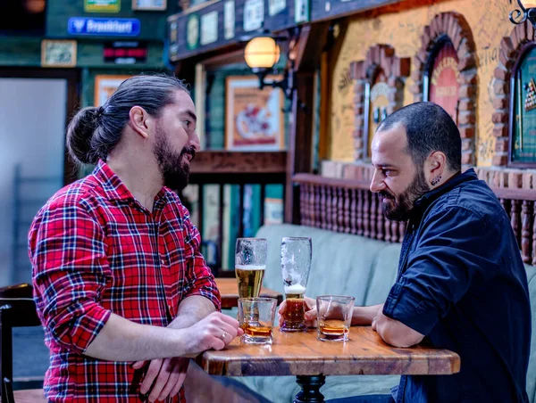 Two male friends drinking whiskey and beer together at the pub. They are drunk and they are talking, and comforting each other.