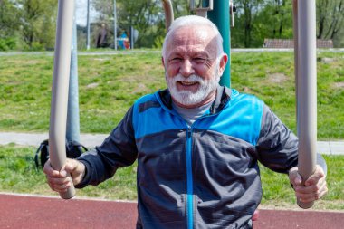 Mutlu ve yorgun yaşlı adam açık havada halka açık spor aletleri üzerinde egzersiz yapıyor..