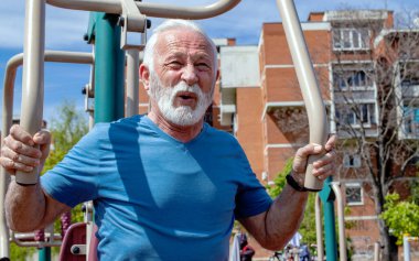 Yorgun bir son sınıf öğrencisi açık havada spor aletleri üzerinde egzersiz yapıyor..