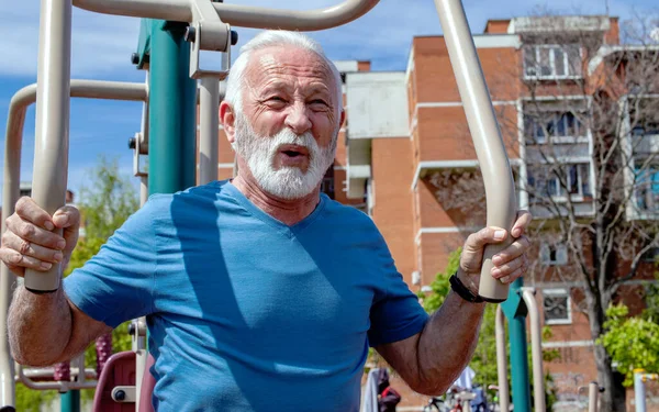 Yorgun bir son sınıf öğrencisi açık havada spor aletleri üzerinde egzersiz yapıyor..