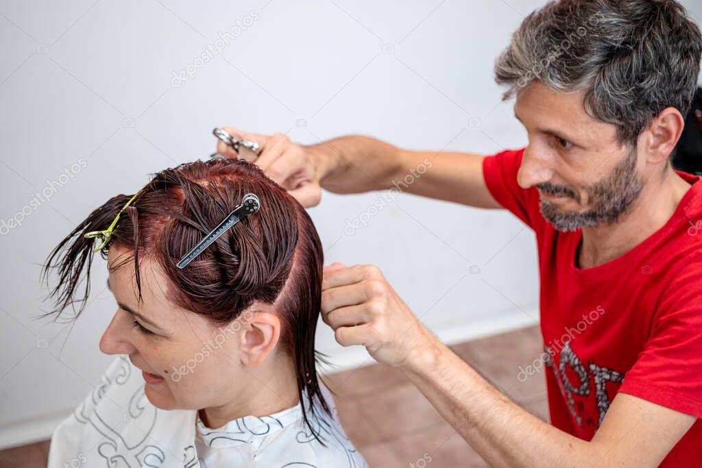 Young female customer getting her haircut by a professional hairstylist at a beauty or hairdresser salon. Hand with scissors arranging the wet hair.