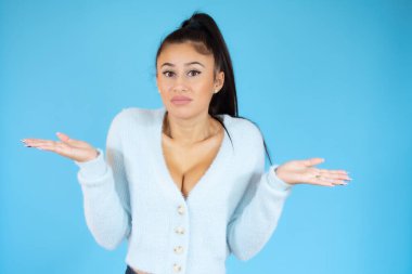 Mavi soyutlanmış arka planda duran genç bir kadın kollarını açmış soru sormayı, düşünceli ifadeyi düşünüyor. Şüphe kavramı.