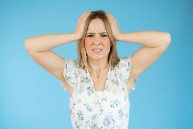 Kafasına dokunan sarı saçlı genç bir kadının portresi ve mavi arka planda izole edilmiş endişelerini ifade ediyor.