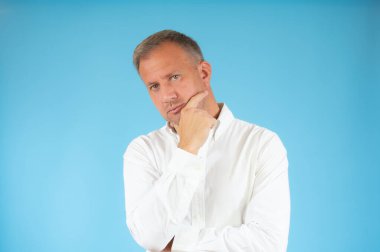 Sıradan gömlekli genç adam mavi arka planı düşünüyor..