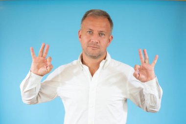 Mavi gözlü, gülümseyen, el ve parmaklarıyla imza atan genç, yakışıklı bir adam. Başarılı ifade.