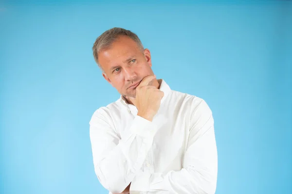 Sıradan gömlekli genç adam mavi arka planı düşünüyor..