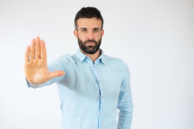 Mavi gömlekli genç adam beyaz arka planda el hareketini durduruyor..
