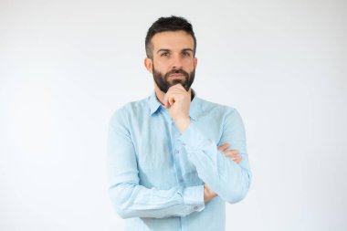 Genç adam, beyaz arka planda şüpheli davranışlar sergileyen sıradan mavi bir gömlek giyiyor..