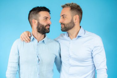 Gündelik kıyafetler giyen, mutlu ve olumlu bir şekilde sarılan, kendinden emin gülümseyen iki genç gay. Sevgi ve özgüven.