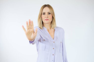 Beyaz arka planda izole edilmiş dur hareketi gösteren elini uzatmış ciddi bir beyaz kadının portresi.