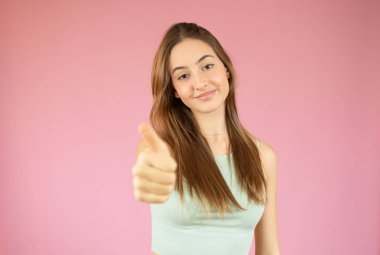 Mutlu üniversite öğrencisi pembe arka planda başparmak gösteriyor.