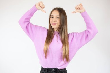 Kendini işaret eden genç bir kadın, beyaz arka planda izole edilmiş beyaz süveter içinde gülümsüyor. İnsanlar samimi duygular, yaşam tarzı konsepti.