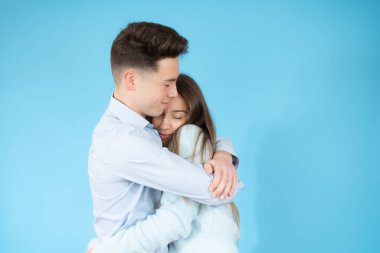 Mavi arka planda birbirini kucaklayan genç çift.