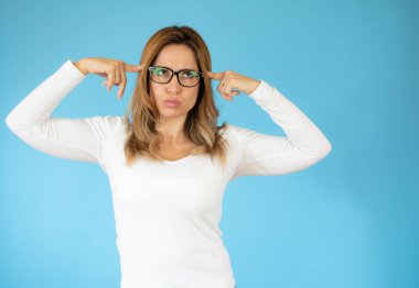 Genç, güzel bir kadın düşünüyor, kuşkulu ve şaşkın hissediyor, farklı seçenekleri var, mavi duvara karşı hangi kararı vereceğini merak ediyor.