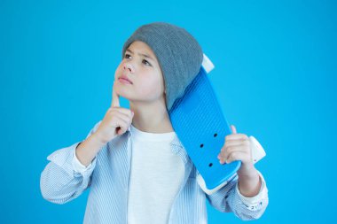 Mavi arka planda kaykay tutan sıradan giysili dalgın bir adamın portresi.,