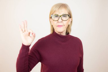 Gülümseyen yaşlı bayan beyaz arka planda mükemmel bir işaret veriyor..