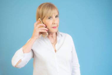 Gülümseyen son sınıf kadınları mavi arka planda cep telefonu kullanıyorlar..