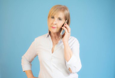 Gülümseyen son sınıf kadınları mavi arka planda cep telefonu kullanıyorlar..