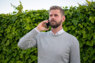 Genç adam dışarıda duruyor, telefonda konuşuyor..