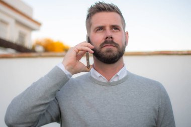 Genç adam dışarıda duruyor, telefonda konuşuyor..