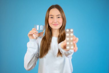 Genç ve güzel bir kız mavi arka planda ağız ilacı ve su alıyor.