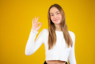 Genç mutlu kadın sarı arka planda baş parmağını gösteriyor.