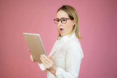 Gülümseyen genç kadın pembe arka planda dijital tablet tutuyor.