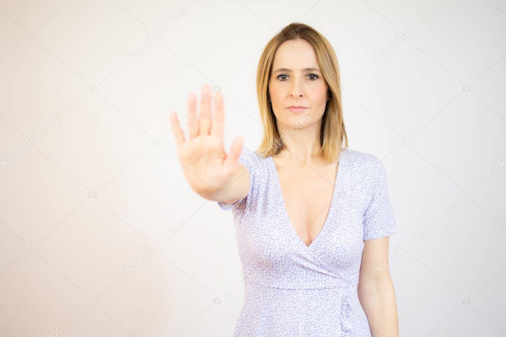 Young woman making stop sign with hand, saying no, looking at camera over white background.