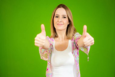 Gülümseyen güzel genç bir kadın yeşil arka planda baş parmak gösteriyor.