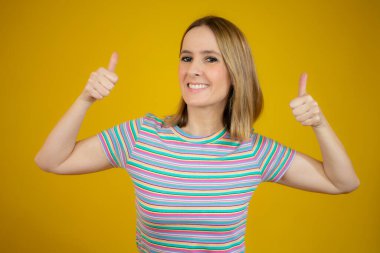Gülümseyen güzel genç kadın sarı arka planda baş parmak gösteriyor.