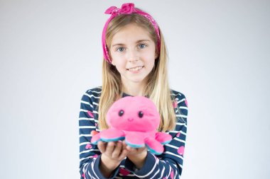 Uzun saçlı, çizgili tişörtlü, elinde ahtapot oyuncağı olan mutlu bir beyaz kız..