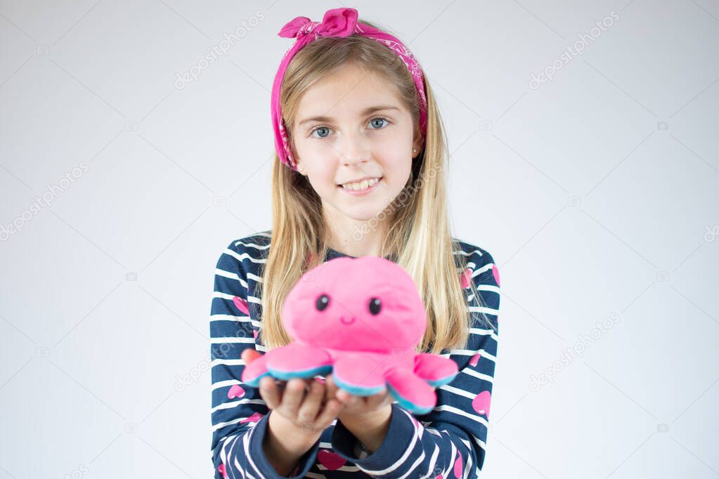 Little caucasian girl with long hair wearing striped shirt and holding octopus toy smiling happy.