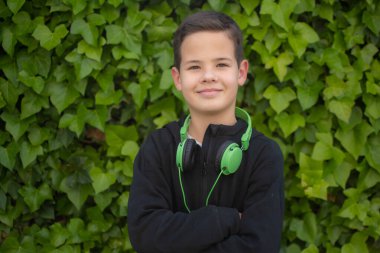 Kulaklık takan, kolları bağlı kameraya bakan, gülümseyen bir çocuk..