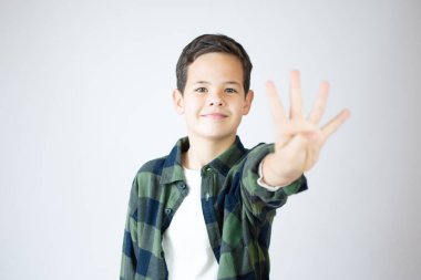 Beyaz duvarın önünde duran, dört numaralı parmaklarıyla işaret eden, kendinden emin ve mutlu gülümseyen beyaz çocuk..