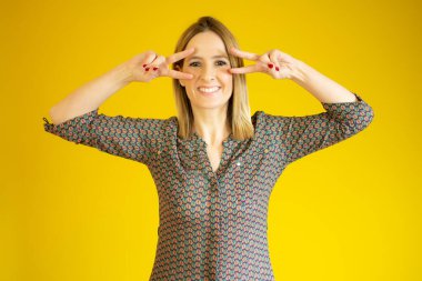 Arka planda kalmış genç bir kadın gülümsüyor ve zafer işareti gösteriyor.