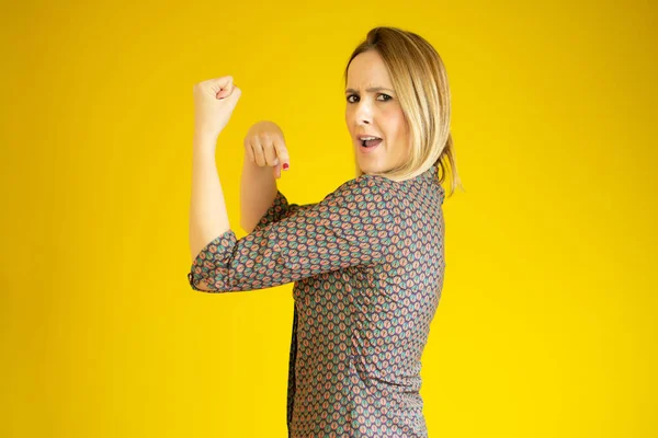 Successful woman raising hand in success gesture over yellow background