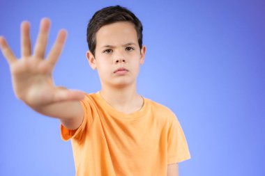 İzole edilmiş mor arka planda duran sıradan tişörtler giyen güzel çocuk avucunun içi gibi şarkı söylemeyi kesiyor. Yüzünde olumsuz ve ciddi bir jest olan uyarı ifadesi.