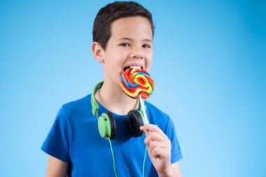 Mavi arka planda kulaklıkla lolipop yiyen bir çocuğun yakın çekimi.