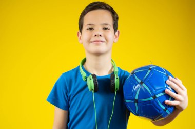 Mavi bir top tutan ve yeşil kulaklık takan genç bir çocuk.