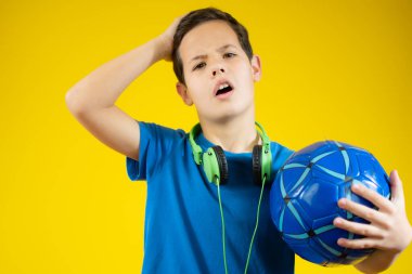 Genç bir çocuk mavi bir top tutuyor ve yeşil kulaklık takıyor.