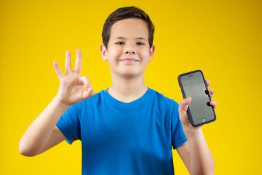 Beyaz çocuk sarı arka planda izole edilmiş bir telefonla iyi niyet gösterisi yapıyor.