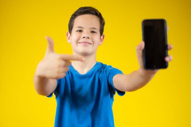 Beyaz çocuk sarı arka planda izole edilmiş bir telefonla iyi niyet gösterisi yapıyor.
