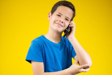 Sarı arka planda akıllı telefonuyla konuşan mutlu küçük bir çocuğun yakın çekimi.