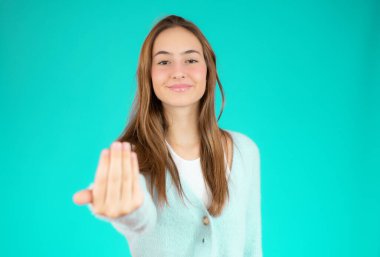 Genç ve güzel bir kadın, kendinden emin ve gülümsüyor. Elleriyle jest yapıyor. Olumlu ve arkadaş canlısı.