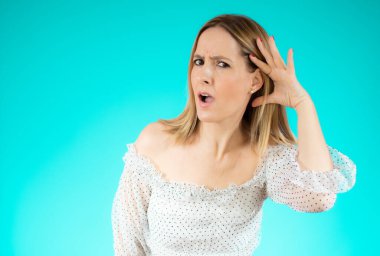 Yalıtılmış yeşil arka planda genç bir kadın. Kulağına elini sürerek bir şeyler dinliyor.