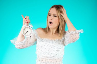 Genç ve güzel bir kadın yeşil arka planda sürpriz bir jest yaparak saati tutuyor..