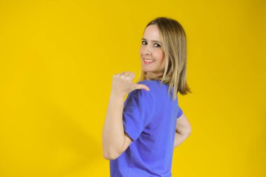 İzole edilmiş sarı arka planda genç bir kadın parmak işareti yapıyor.